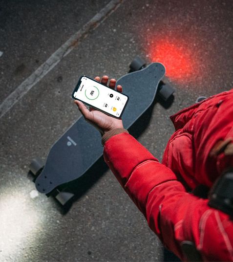 A hand holding a phone app above an electric skateboard